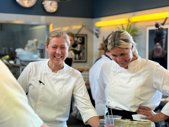 Sarah Rom Gjerø og værkstedsmester Kathrine Foged Thomsen står side om side i kokketøj og griner sammen i skolens Dessertværksted.