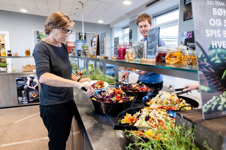 Personer tager mad fra en buffet i en moderne kantine.