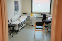 Lægeklinik med undersøgelsesbriks, stole og skrivebord.