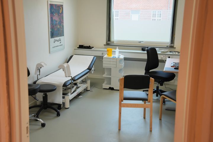 En tom lægeklinik med undersøgelsesbriks, stole og skrivebord.