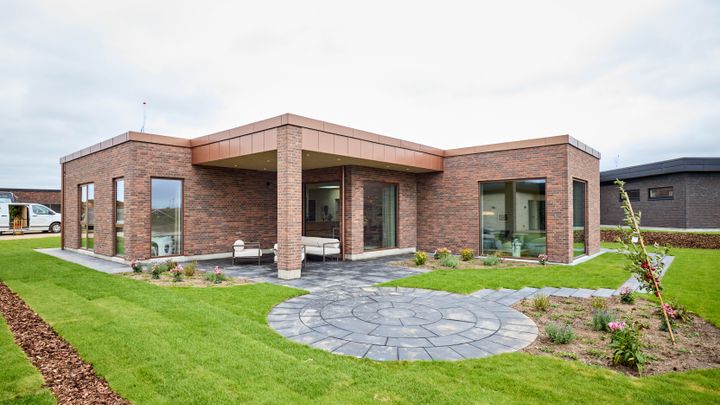 Lokalplanen i Margrethehøj åbner for en bred vifte af arkitektoniske muligheder. Her er en moderne HusCompagniet-villa med fladt tag, overdækket terrasse og varme teglsten, der falder naturligt ind i de grønne omgivelser.