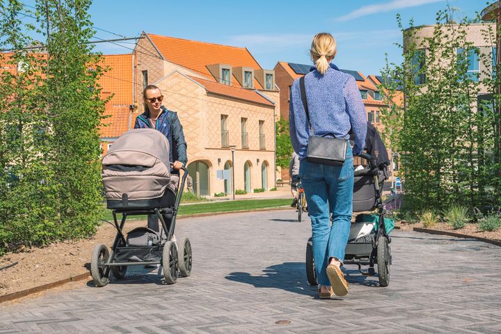 To yngre kvinder med barnevogne passerer hinanden på en flisebelagt sti i en park.