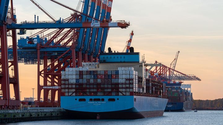 Containerskib i solnedgang er ved at blive losset af kæmpekraner på havn.