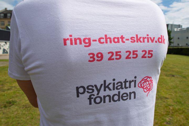 BIllede af en ung mand i t-shirt med påskrift om telefonnummer og link til Psykiatrifondens rådgivning.