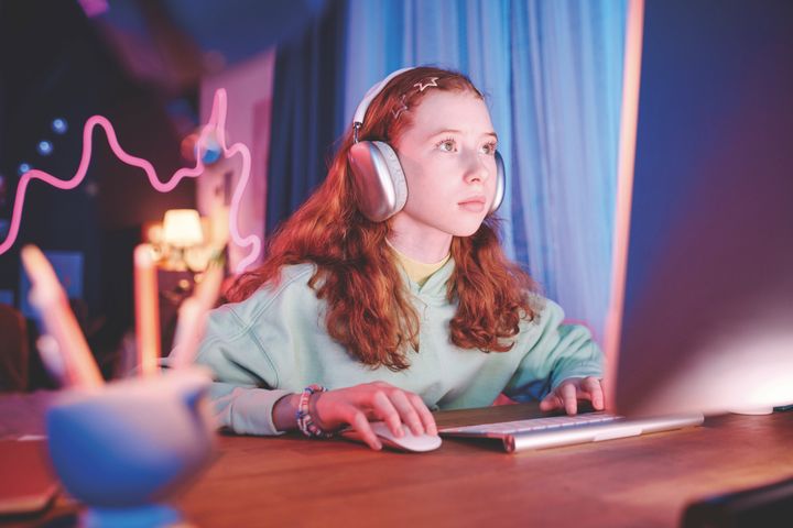 Pige ses forfra siddende foran computer, der lyser hendes ansigt op.