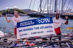 De to roere med et flag mellem sig med tekst, der siger, at de har roet tværs over Atlanterhavet.