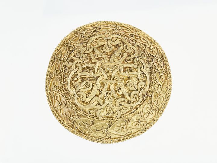 Dragtspænde af guld. Skatten er fundet tæt ved Varde i 1892. Den indeholder en armring og to dragtspænder af guld. De to spænder er blandt de fineste eksempler på guldsmedekunst fra Danmarks vikingetid.