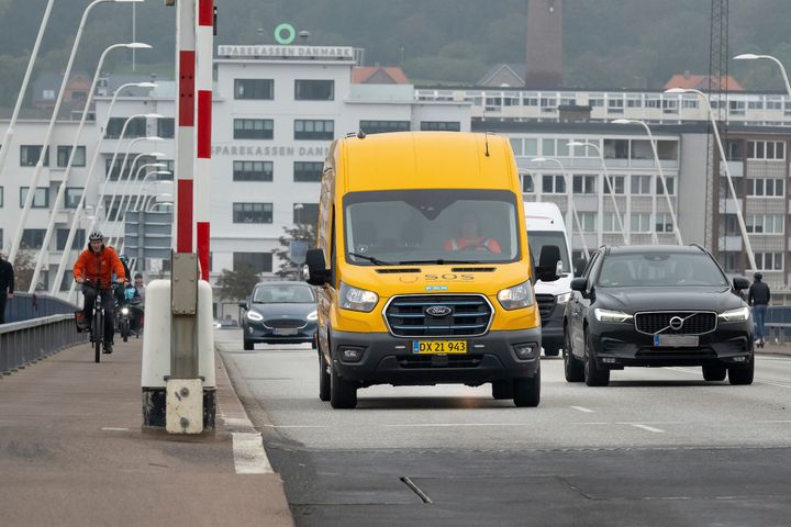 Gul servicebil fra SOS Dansk Autohjælp kører på en bro.