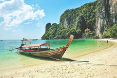 En traditionel træbåd på en smuk thailandsk strand med turkis vand og frodig baggrund.