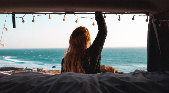 Kvinde ser ud over havet fra en campervan.