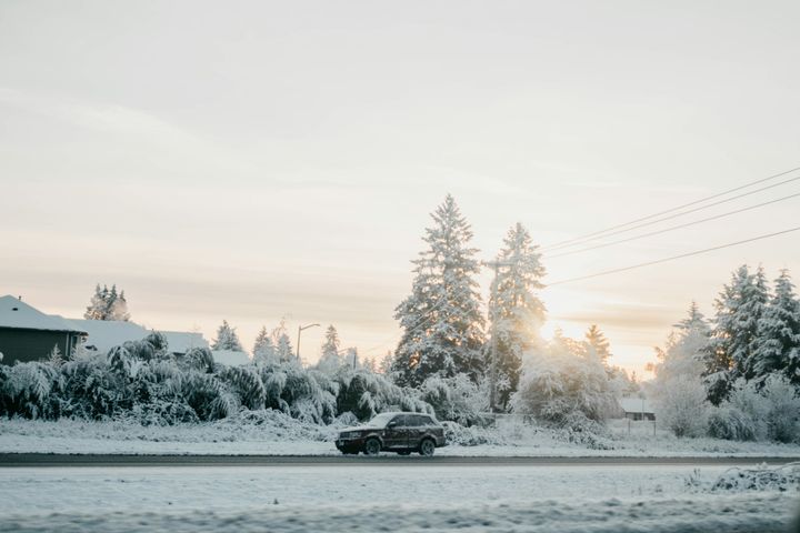 En bil kör på en snötäckt väg kantad av snötyngda träd under en ljus vinterhimmel.