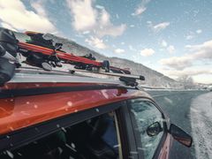 Bil med skidor på taket på en snöig väg.