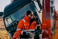 En person i orange arbetskläder står framför en lutande lastbil och talar i en radio.