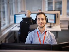 Ung man med headset arbetar vid dator i kontorsmiljö.