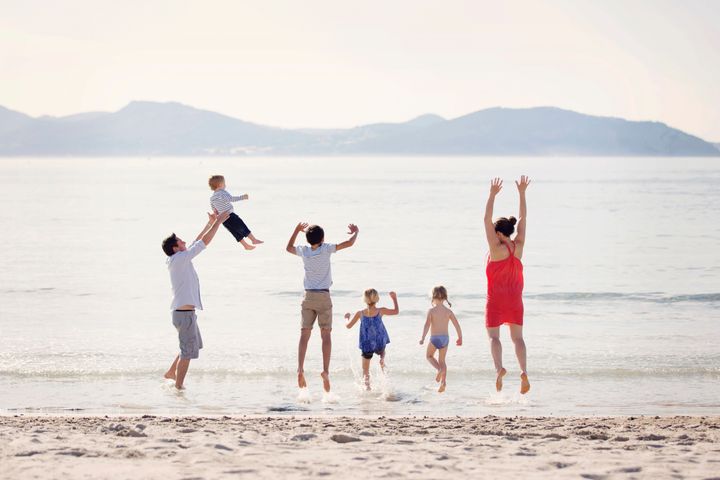 En familie leker og hopper på en strand ved sjøen.