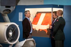 Hans Majestæt Kongen står foran resterne af det danske flag, der stod på Hans Ø. TV. ses Krigsmuseets chef David Høyer og TH. chef for Slædepatruljen SIRIUS, Christopher Sohl. Foto: Thorkild Jensen.
