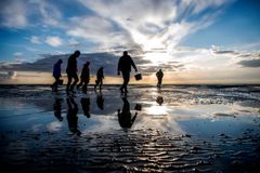 Personer går på en strand ved solnedgang med skyer spejlet i vandet.