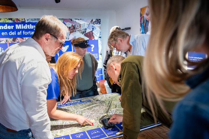 Deltagere i byværksted diskuterer byplanlægning over et kort.