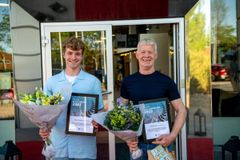 To personer holder blomster og priser uden for en bygning.