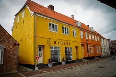 Et gult og orange bageri med en dansk flag foran, beliggende på en brostensbelagt gade.