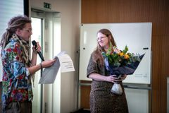 Person modtager blomster og diplom ved en ceremoni.