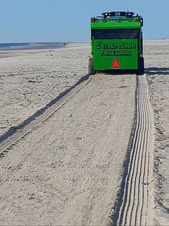 En rengøringsmaskine kører på en strand, hvor sandet er forurenet med små olieperler.