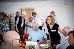 En gruppe mennesker deltager i en social sammenkomst omkring et bord med mad og drikke.