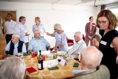 En gruppe mennesker sidder og står omkring et bord ved en social begivenhed.