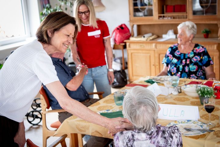 En kvinde hilser på en ældre dame ved et bord med andre deltagere.