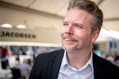 En smilende mand i jakkesæt står udendørs.