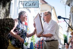 Et ældre par står foran en café. Kvinden modtager et diplom fra manden.
