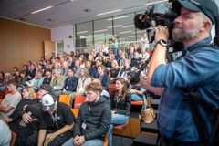 En stor gruppe mennesker sidder i et fyldt auditorium, mens en fotograf optager begivenheden.