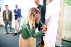 En person underskriver et stort papirark, mens tre personer ser på i baggrunden.