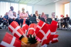 En gruppe mennesker sidder i et mødelokale med danske flag i forgrunden.