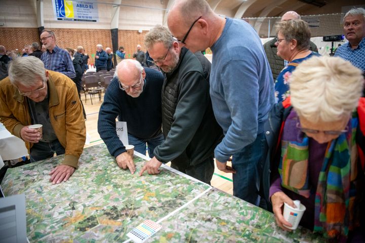 Gruppe mennesker samles omkring et stort kortbord ved et møde.