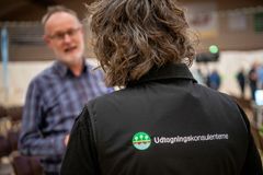 Person taler med en anden under en konference, iført en jakke med "Udtagningens konsulenterne" logo.