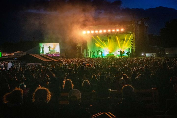 En stor menneskemængde nyder en koncert om natten med farverige lys på scenen.
