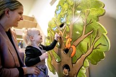 En to-årig pige lægger sin sut i et suttetræ, mens en voksen ser på.