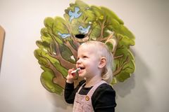 Lille barn børster tænder foran en vægdekoration med træ og fugle.