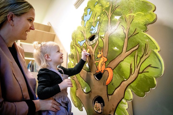 En to-årig pige lægger sin sut i et suttetræ, mens en voksen ser på.
