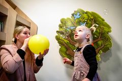 En voksen og et barn laver sæbebobler foran en vægdekoration med et træ.