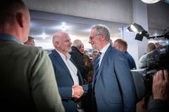 To mænd i jakkesæt giver hinanden håndtryk i en menneskemængde.