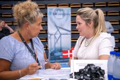 To kvinder sidder ved et bord og taler sammen på en messe.