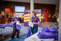 To medarbejdere i lilla poloer står ved en stand med foldere og lilla stofposer ved Bo- og jobmesse i Sønderjylland.