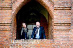 To personer står i en bue af en murstensbygning og smiler mod kameraet.