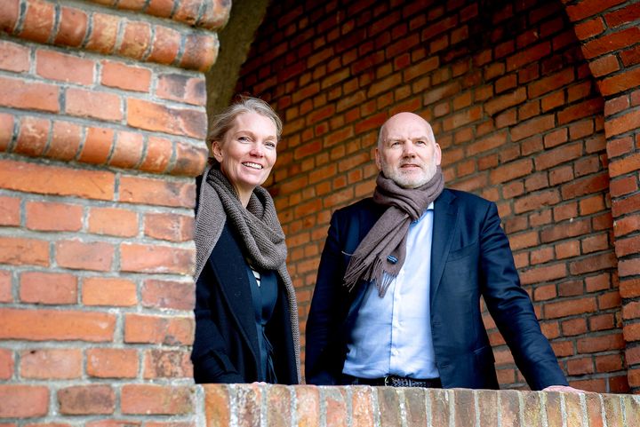 To personer står ved en murstensvæg og kigger ud.