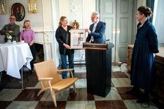 Person modtager en pris ved en ceremoni i et elegant rum. En Wegner-stol er i forgrunden.