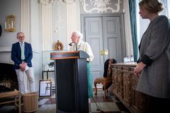 Ældre person holder tale ved podie i traditionelt indrettet rum med tilhørere.