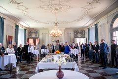 En større gruppe mennesker er samlet i en elegant sal med stukloft og lysekrone til Wegner Prisuddelingen på Schackenborg Slot.