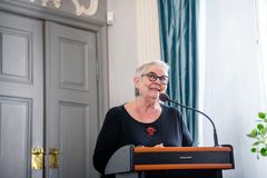 En kvinde taler ved en talerstol i et formelt rum.